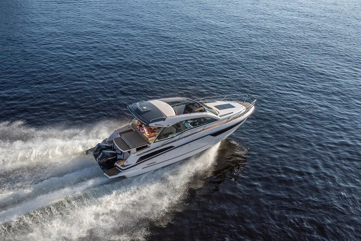 A white motorboat speeds across calm blue water, with a person visible in the driver's seat enjoying a sunny day.
